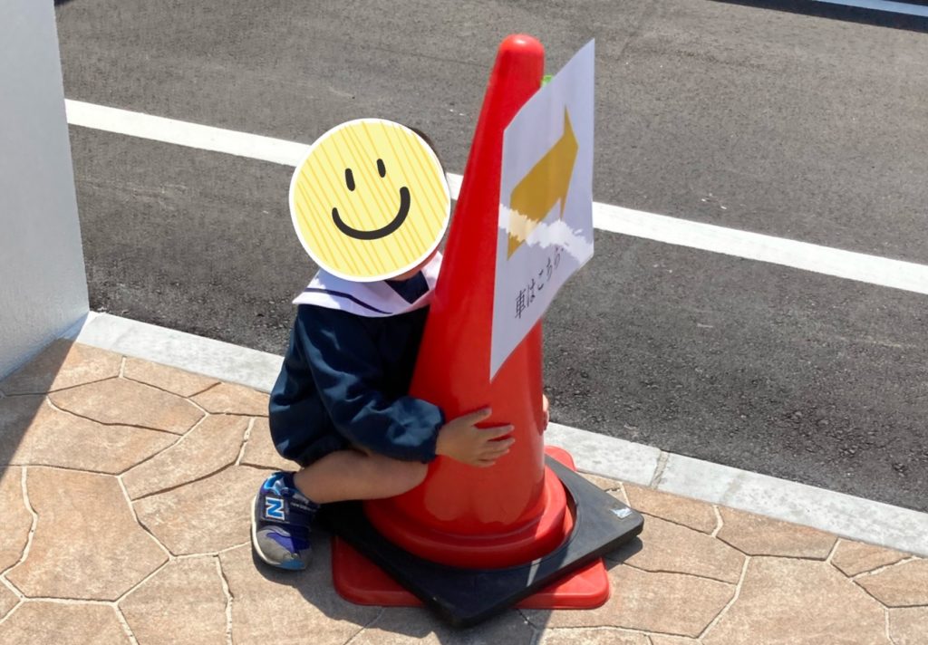 子どもが赤いコーンにつかまって座っている。